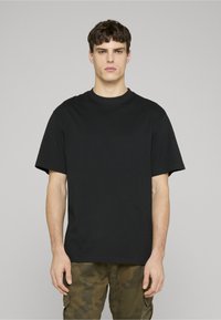 Černé bavlněné tričko s klasickým kulatým výstřihem a krátkými rukávy, s volným střihem a minimalistickým designem. Nosit s maskáčovými kalhotami.