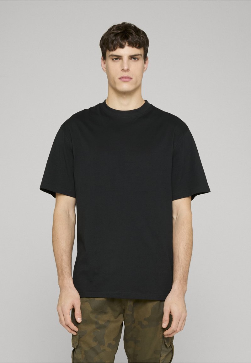 Černé bavlněné tričko s klasickým kulatým výstřihem a krátkými rukávy, s volným střihem a minimalistickým designem. Nosit s maskáčovými kalhotami.