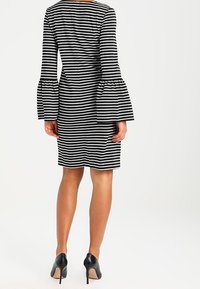 Nainen, joka pitää päällään musta-valkoista vaakaraitapukua, jossa on leveät pitkät hihat ja mustat korkokengät, yllä olevana.