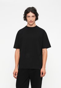 Camiseta negra de manga corta hecha de algodón, con un corte relajado, escote redondo y diseño minimalista. Sin patrones ni gráficos visibles.