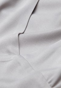 Ljusgrått tyg med en slät textur, med mjuka draperingar och subtila veck, som visar en mjuk, vävd design.