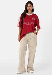 Rode oversized t-shirt met witte accenten en logo, gecombineerd met beige wijde broek. Glad stof met contrasterend kraagontwerp.