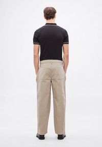 Fekete galléros póló fehér szegéllyel; bézs, széles szárú nadrág; sima textúra; két hátsó zseb; fekete cipővel viselve.