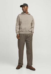 Beige hooded sweatshirt with a front pocket, paired with brown pleated trousers and brown shoes. Black cap worn on the head.