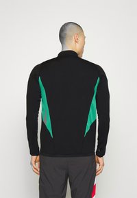 Camiseta atlética de manga larga negra con paneles decorativos en verde y gris a los lados. Confeccionada con una tela elástica y un diseño ajustado.
