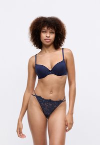 Soutien-gorge bleu marine en matériau lisse avec un petit nœud ; string en dentelle assorti avec des fines bretelles et des accents floraux.