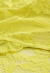 Tissu en dentelle jaune avec broderie florale et motif en maille, légèrement froissé et superposé.