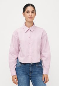 Cropped pink shirt with vertical white stripes, button-up front, large collar, and long sleeves with striped cuffs. Paired with blue jeans.