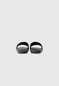 Black slide sandals with a smooth matte texture, featuring two wide straps and a flat sole. Minimalist design with no visible logos.