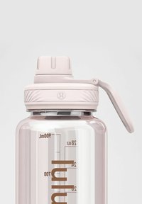 Przezroczysta plastikowa butelka na wodę w różowym odcieniu, z szerokim otworem, matową beżową nakrętką i uchwytem do łatwego przenoszenia.