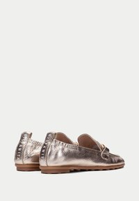 Mocassini dorati metallici con pelle texturizzata, suole in gomma piane e un piccolo tab posteriore. Presentano una cintura decorativa e un marchio distintivo.