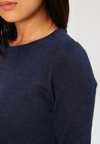 Navy blue knit sweater featuring a round neckline and long sleeves, with a soft texture and a fitted silhouette.