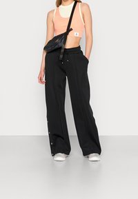 Czarne spodnie o szerokich nogawkach z guzikami po bokach, w połączeniu z jasnoróżowym topem w stylu crop i czarną torbą na ramię. Gładki materiał, casualowy design.