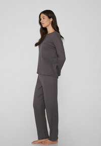 Šedý loungewear set obsahuje top s dlouhým rukávem a odpovídající kalhoty s ribbovanou texturou, což zajišťuje pohodlný a casual vzhled.