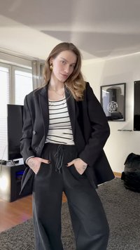 Svart oversized blazer over en hvit og svart stripete topp, kombinert med svarte vide bukser med elastisk midje og snor.