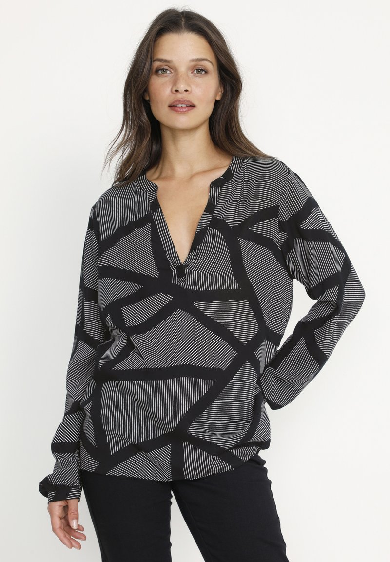 Black and white long-sleeve blouse featuring a deep V-neck, with a geometric linear pattern throughout and relaxed fit.