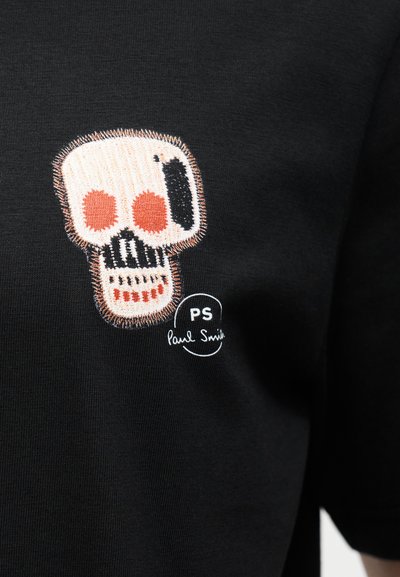 Κεντημένο στυλιζαρισμένο κρανίο με κόκκινες κόγχες ματιών και δόντια σε μαύρο ύφασμα, συνοδευόμενο από το λογότυπο «PS Paul Smith».