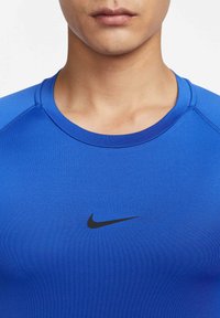 Blå treningsskjorte laget av et glatt, elastisk materiale. Har rund hals og en liten svart Nike-logo på brystet.