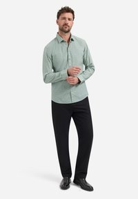 Lichtgroen overhemd met knopen, voorzien van een geometrisch patroon, lange mouwen en een gestructureerde kraag, gecombineerd met zwarte broek en glanzende zwarte schoenen.