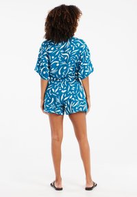 Rompers à motif bleu présentant des formes abstraites blanches, manches courtes, taille à cordon de serrage et design de short. Tissu texturé avec une coupe décontractée.