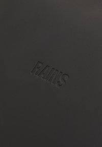 Schwarzes strukturiertes Material mit einem geprägten "RAINS"-Logo, das ein minimalistisches Design und eine glatte Oberfläche ohne zusätzliche Muster oder Akzente präsentiert.