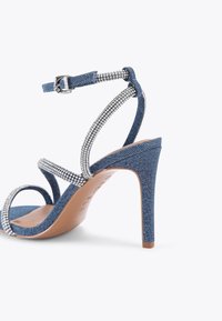 Sandały na obcasie z denimowego materiału o strapowym designie, ozdobione cyrkoniami wzdłuż pasków, z eleganckim obcasem typu stiletto i beżową wkładką.
