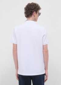 Polo blanc avec col et manches courtes, au design épuré. Le dos est uni avec un tissu légèrement texturé.