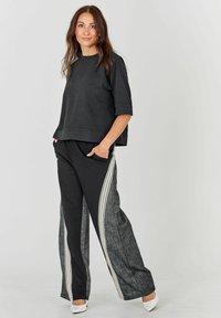 Hanorac scurt cu mâneci scurte, de culoare neagră, cu un croi lejer, se asortează cu pantaloni negri care prezintă un panou lateral texturat de culoare gri și dungi albe pe picioare.