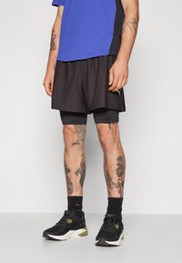 Vyrų sportinė apranga, kurioje matomas mėlynas trumpas rankovėmis marškinėlis, juodos šortai ir juodi sportiniai bateliai su žaliais akcentais. Matomos blauzdų tatuiruotės.