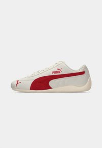 Sneaker in suede crema con dettagli rossi, caratterizzati da un design testurizzato e una suola in gomma. Logo visibile in modo prominente sul lato.