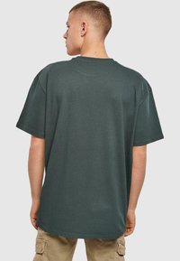 Tmavě zelené, oversized tričko z ribového materiálu, s kulatým výstřihem a krátkými rukávy, viděné z boku.