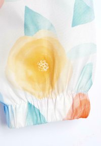 Tissu à motifs floraux avec des accents jaunes, bleu clair et corail. Texture douce, poignet élastique froncé en bas, couleurs vives.