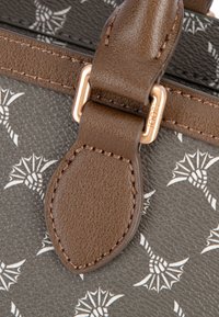 Brązowy pasek ze sztucznej skóry z mosiężnymi okuciami i wytłoczonym wzorem ananasa na ciemnoszarym tle. Widoczny jest detal o teksturowanym wykończeniu.