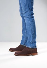 Bruine suède enkellaarsjes met elastische zijpanelen, gecombineerd met strakke blauwe spijkerbroeken. De laarsjes hebben een gladde houten zool.