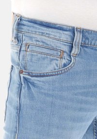 Jeans de mezclilla azul claro con un ajuste Slim, que cuentan con un pequeño bolsillo trasero y costuras en contraste, mostrando una textura suave.