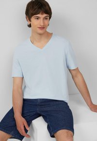 Lichtblauw V-hals T-shirt van zacht materiaal, met korte mouwen en een ontspannen pasvorm. Draagt het met donkerdenim shorts, zittend op een witte ondergrond.