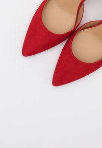 Paire de chaussures plates rouges à bout pointu avec semelles intérieures couleur naturel, vues de dessus sur un fond gris clair.