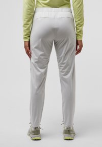 Witte sportbroek met een tapered fit, elastische tailleband, zijnaad en kleine ventilatiegaten, gecombineerd met grijze schoenen en een groene top.