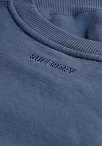 Blauwe sweatshirt met geribde halslijn en geborduurd "SUPERDRY" logo in bijpassende kleuren op de borst. Zachte stoftextuur.
