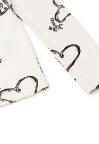 Top in tessuto a coste bianco con motivi a forma di cuore neri e testi. Include un'etichetta piccola sull'orlo. Maniche lunghe con polsini.