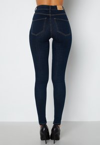 Vysoké tmavě modré džíny se slim fit, které mají dvě zadní kapsy a kontrastní švy. V kombinaci s černými vysokými podpatky.