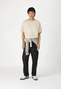 Šviesiai rudos trumpomis rankovėmis marškiniai, juodos krovinių kelnės su kišenėmis ir pilkos dryžuotos audinio juostelės surištos aplink juosmenį. Sportbačiai su juodais ir šviesiai rudos spalvų akcentais.