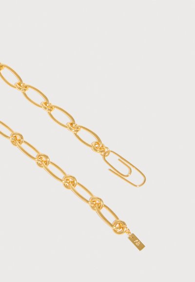 Χρυσό κολιέ με αλυσίδα από επιμηκυμένους οβάλ κρίκους και κούμπωμα που μοιάζει με μεγάλο χρυσό συνδετήρα σε ανοιχτό φόντο.
