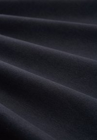 Tessuto nero con una superficie liscia e leggermente texturizzata, disposto in pieghe ondulate, che mette in evidenza un colore uniforme e una tessitura coerente.