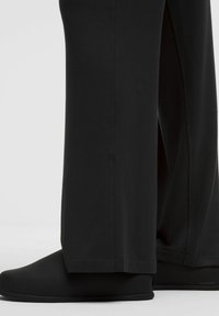 Fekete sportnadrág laza szabással és oldalsó hasítékokkal, sima matt felületű, elegáns fekete slip-on cipővel párosítva.