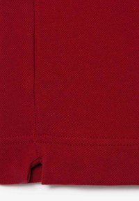 Röd texturerad tyg med ett subtilt diagonalt mönster, med en delad fåll och snygg sömnad längs kanterna.