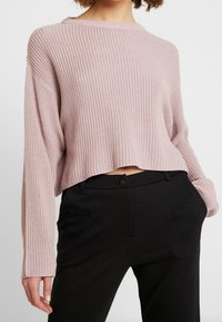 Lichtroze cropped gebreid sweater met een geribbelde textuur, voorzien van verlaagde schouders en een brede halslijn, gecombineerd met op maat gemaakte zwarte broeken.