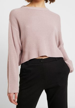 Lys rosa cropped strikket sweater med ribbet tekstur, der har dropped shoulders og en bred halsudskæring, parret med skræddersyede sorte bukser.