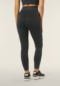 Leggings neri a vita alta con una texture simile al denim e cuciture bianche, dal design aderente e abbinati a scarpe da ginnastica nere.