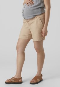 Shorts de un tono beige claro con un corte relajado, que cuentan con una cintura con cordón y bolsillos laterales. Combinados con sandalias marrones de tiras.